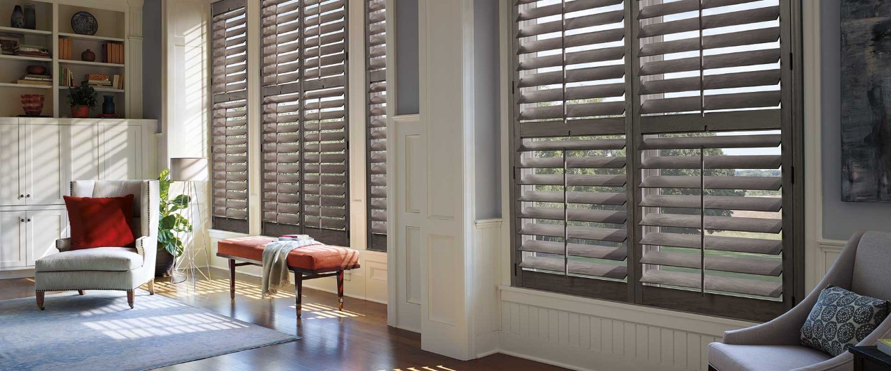 Large sunny windows with accent chair and Heritance Hardwood Shutters.